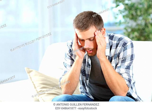 Man suffering headache sitting on a sofa in the living room at home