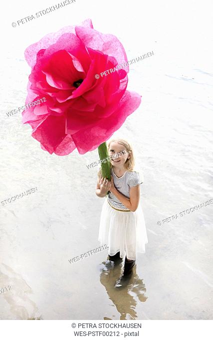 Portrait of smiling blond girl standing in a lake holding oversized pink artificial flower