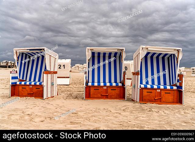 colorful beach baskets on an idyllic golden sand beach on the German Wadden Sea coast under an expressive sky