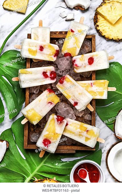 Pina Colada popsicles with candied cherries and pineapple on leaf