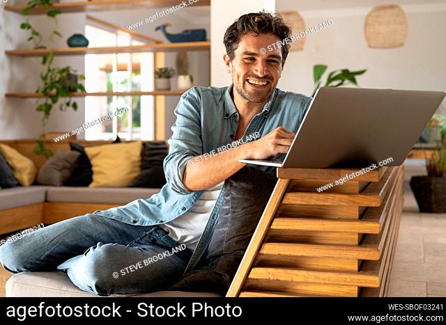 Happy male freelancer using laptop while sitting at home