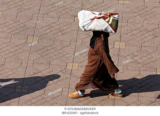 Woman wearing a djellaba carrying a parcel on her head, Djemaa el Fna, Marrakech, Morocco, Africa