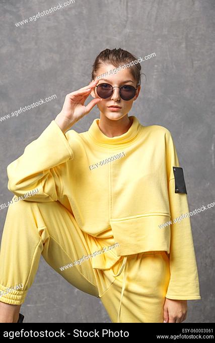 Young woman in yellow sweatshirt and sunglasses on a gray background