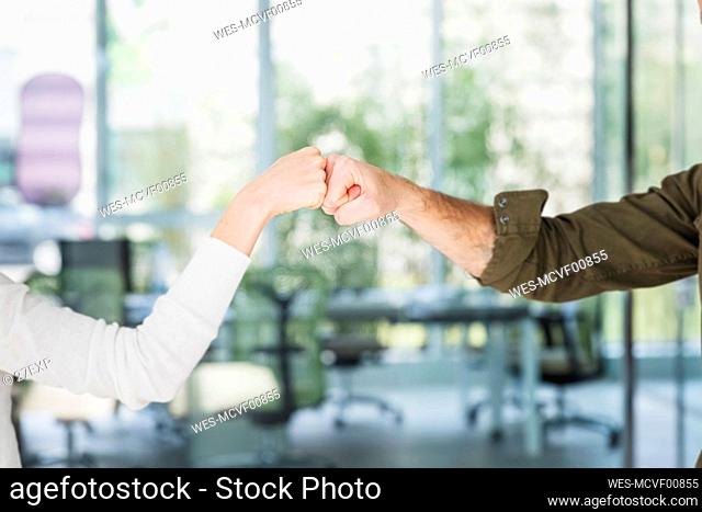 Male and female colleagues greeting with fist bumps in office