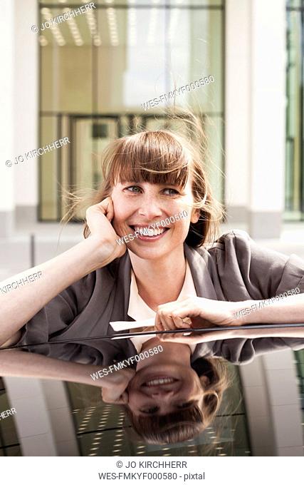 Germany, Hesse, Frankfurt, portrait of smiling businesswoman leaning on car roof
