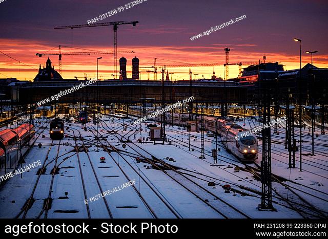 08 December 2023, Bavaria, Munich: The sun rises over the tracks in front of Munich Central Station and the Frauenkirche