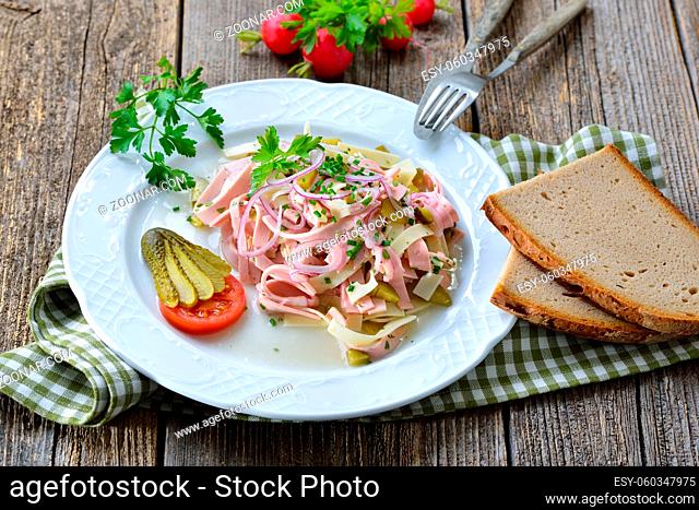 Deftiger Schweizer Wurstsalat mit Käsestreifen und Essiggurken dazu rustikales Bauernbrot ? Hearty sausage salad with cheese strips