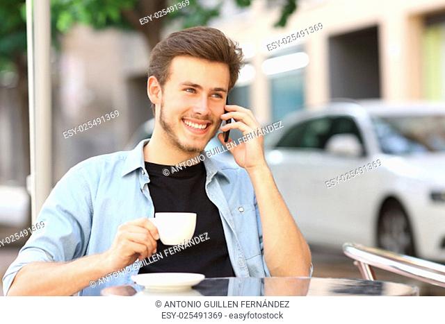 Man talking on the mobile phone in a coffee shop sitting in the terrace outdoors and holding a cup