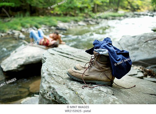 A young man and woman on the rocks on a river bank. Jeans and boots on a rock