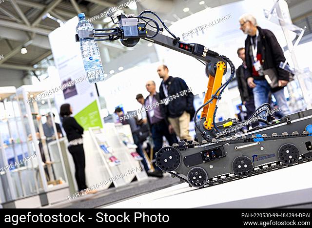 30 May 2022, Lower Saxony, Hanover: The gripper arm of an automated off-road vehicle holds a water bottle at a booth of the Technical University of...