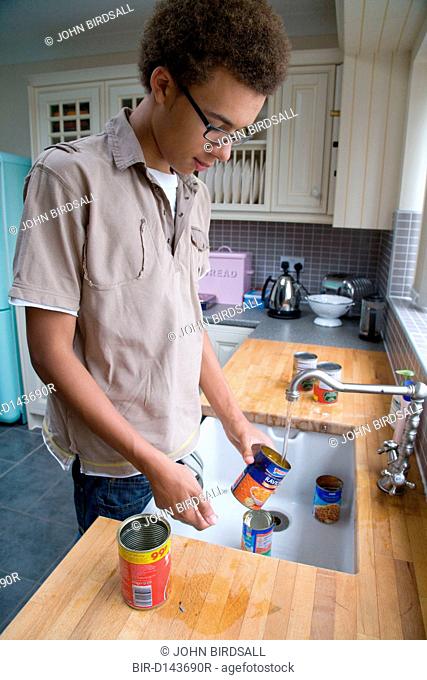Teenage boy rinsing out tins at kitchen sink before putting them out for recycling