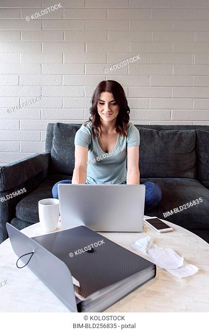 Caucasian woman sitting on sofa using laptop