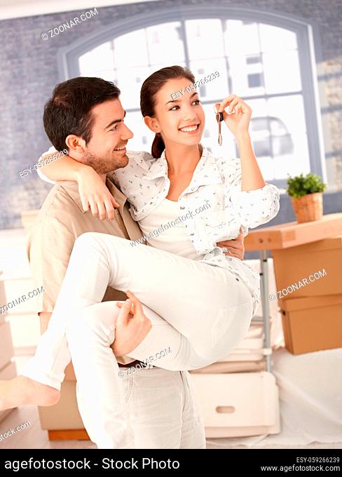 Happy young couple moving to new home, smiling, holding keys in hand