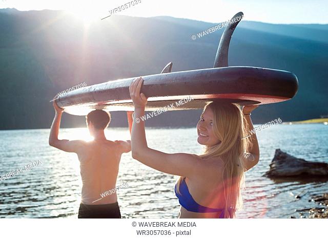 Couple carrying stand up paddle board and walking towards the river