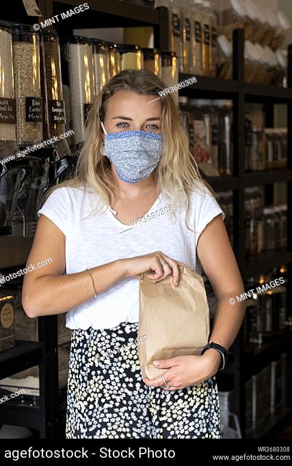 Woman wearing face mask shopping filling a paper bag with loose ingredients