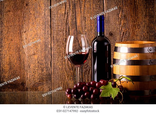 Glass of red wine with bottle barrel grapes on glass with wooden background
