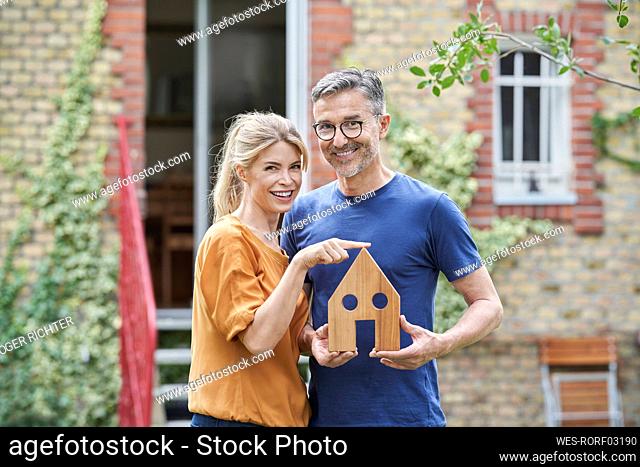 Happy man holding wooden house model by woman in garden