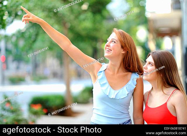 Two happy friends pointing up walking in the street