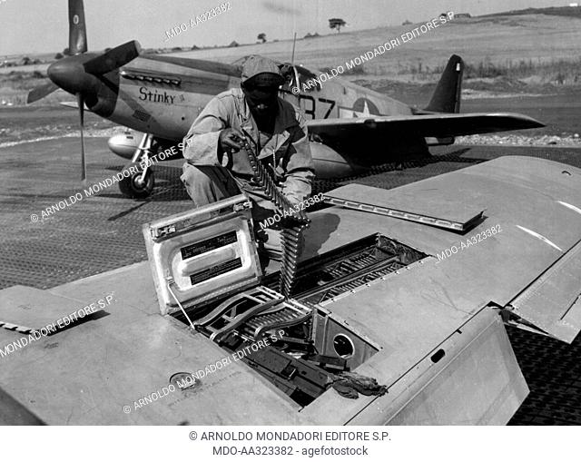 The armament of a U.S. Army aircraft. A U.S. airman checks the munitions of a machine gun on the right wing of a North American P-51 Mustang
