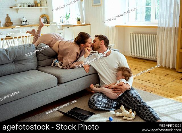 Woman kissing man while daughter sleeping on lap at home