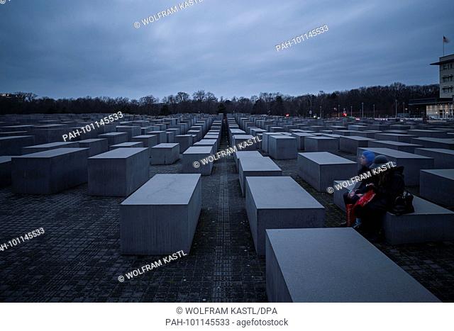 27.01.2018, Germany, Berlin: Tourists sit on a stelae at the Memorial to the Murdered Jews of Europe during International Holocaust Remembrance Day