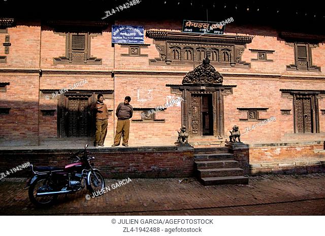 Two men discussing in front of a red brick building, Bhaktapur. Nepal, Kathmandu, Bhaktapur