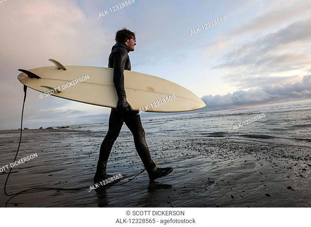 Surfer with board at sunset, Southeast Alaska; Yakutat, Alaska, United States of America