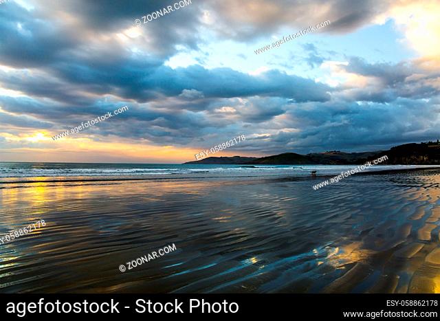 Sunrise over the ocean. Low tide. Strips of sand and water left by the ocean tide. New Zealand, Pacific Coast. The concept of artistic photography