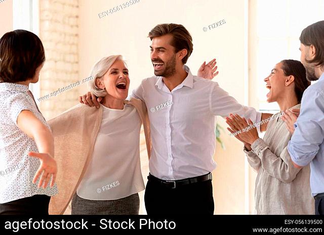 Overjoyed diverse businesspeople hug have fun celebrate shared business success in office together, happy colleagues feel excited triumph after successful work...