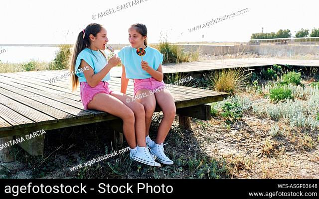 Happy sisters with lollipops sitting on boardwalk