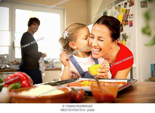 Happy mother and daughter in kitchen preparing pizza with father in background