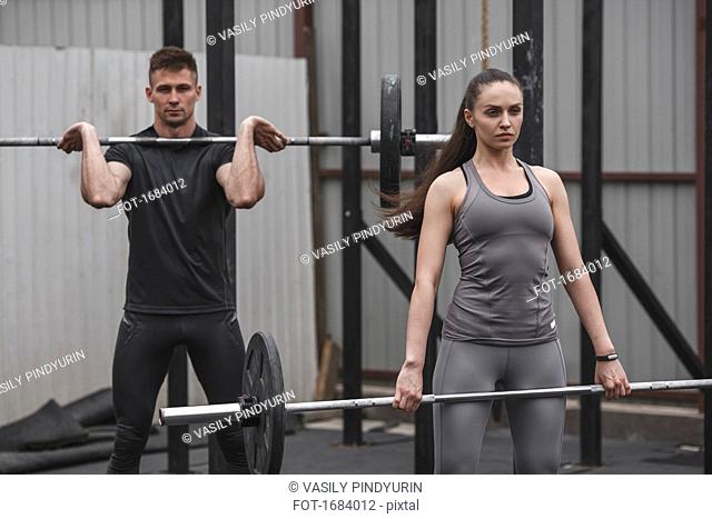 Confident female and male athlete exercising with barbells during crossfit training