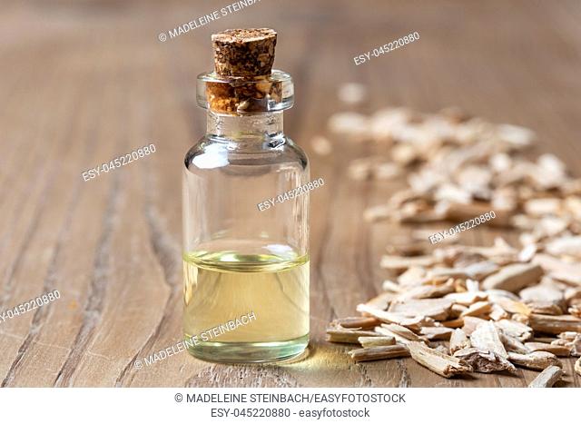 A bottle of essential oil with cedar wood chips on a table