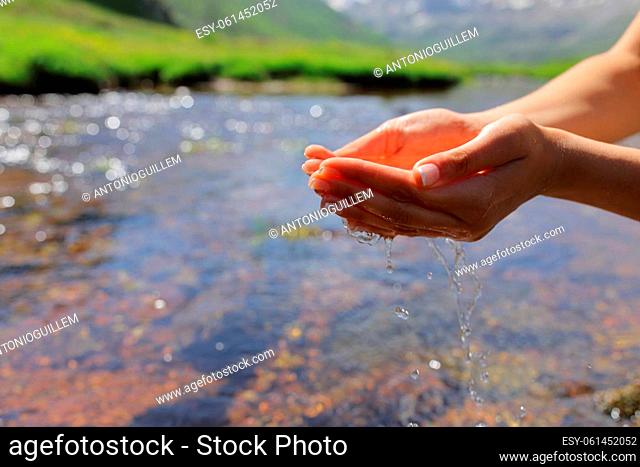 Clos eup portrait of a cupped woman hands catching water in a river in a high mountain