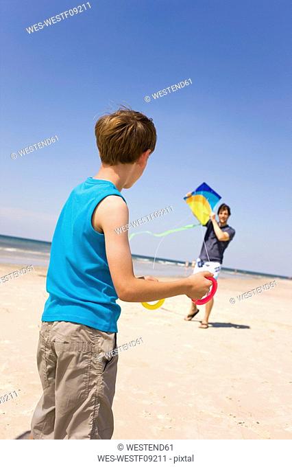 Germany, Baltic sea, Father with son 8-9 flying kite on beach