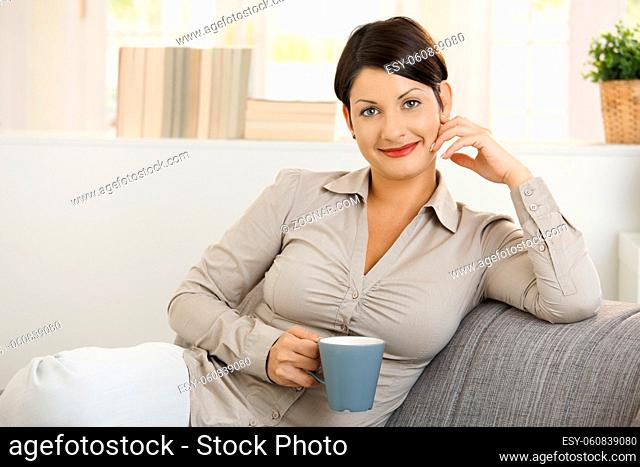 Portrait of young woman drinking coffee at home, smiling