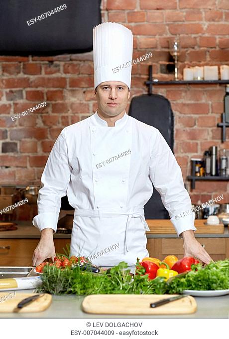 cooking, food and people concept - happy male chef cook with vegetables on restaurant kitchen table