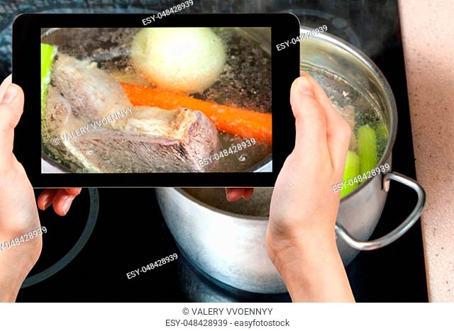 travel concept - visitor photographs of cooking soup with boiling beef broth in steel stewpan close up on caramic stove on smartphone