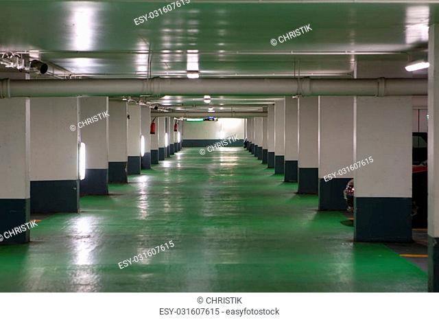 French parking garage with a green floor and white and grey walls. The noses of a couple cars are visable