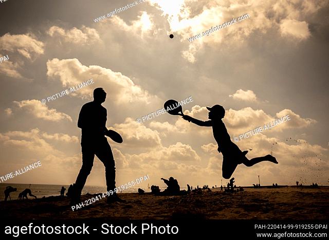 14 April 2022, Lower Saxony, Schillig: A father and his son play beach tennis on the North Sea beach of Schillig in beautiful weather and sunshine
