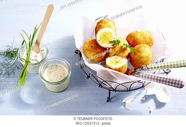 Breaded eggs in parchment paper in a metal basket next to a mustard dip and remoulade