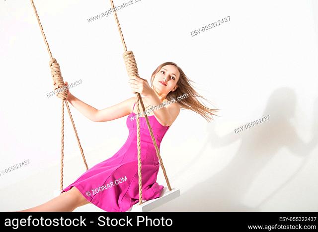 beautiful young blond woman on a swing against white studio background