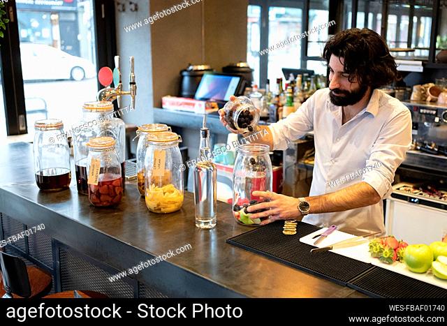 Handsome male bartender putting blackberries in glass jar at bar counter