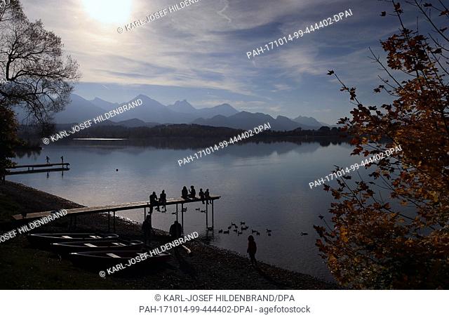 dpatop - Weekend strollers enjoy the Autumn sun as they sit on a jetty at Lake Forggensee in Buching, near Schwangau, Germany, 13 October 2017