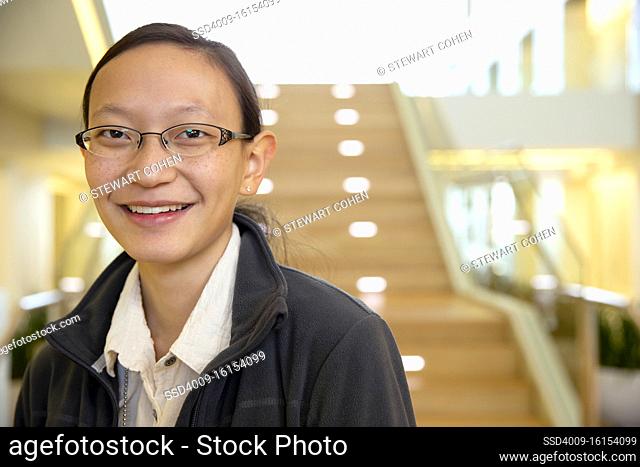 Portrait of young ethnic woman wearing glasses standing by stairwell in lobby of building, smiling looking towards camera