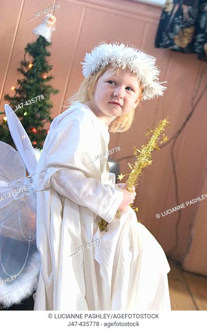 3 year old girl dressed up as an angel, in front of a christmas tree