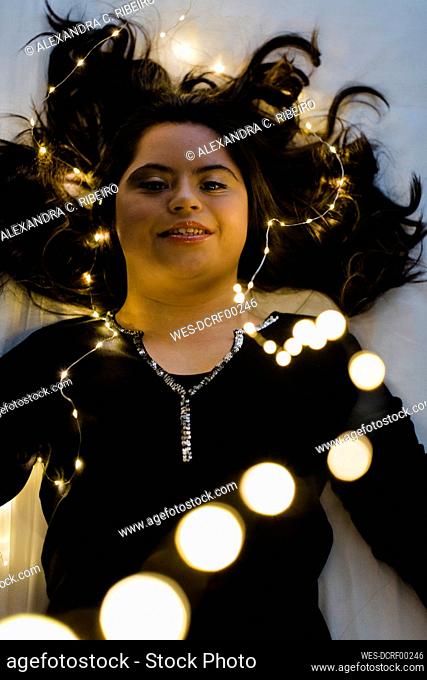 Confident young woman with down syndrome lying on illuminated bed at home