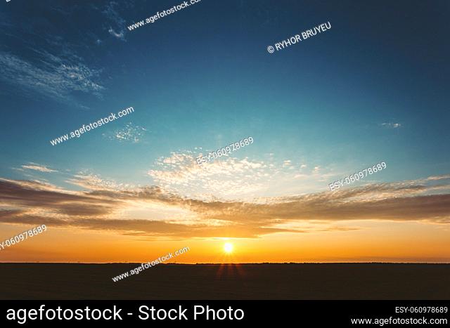 Natural Sunset Sunrise Over Field Or Meadow. Bright Dramatic Sky And Dark Ground. Countryside Landscape Under Scenic Colorful Sky At Sunset Dawn Sunrise