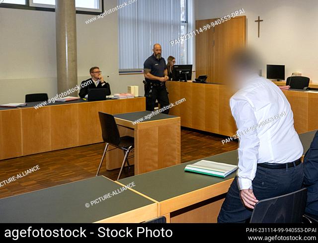 14 November 2023, Bavaria, Augsburg: A man takes a seat in the dock in front of a crucifix in the district court. The accused is the victim's brother