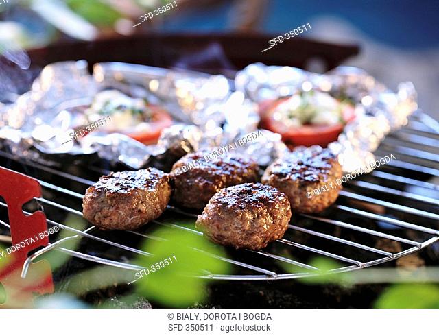 Meatballs and tomatoes in foil on a barbecue
